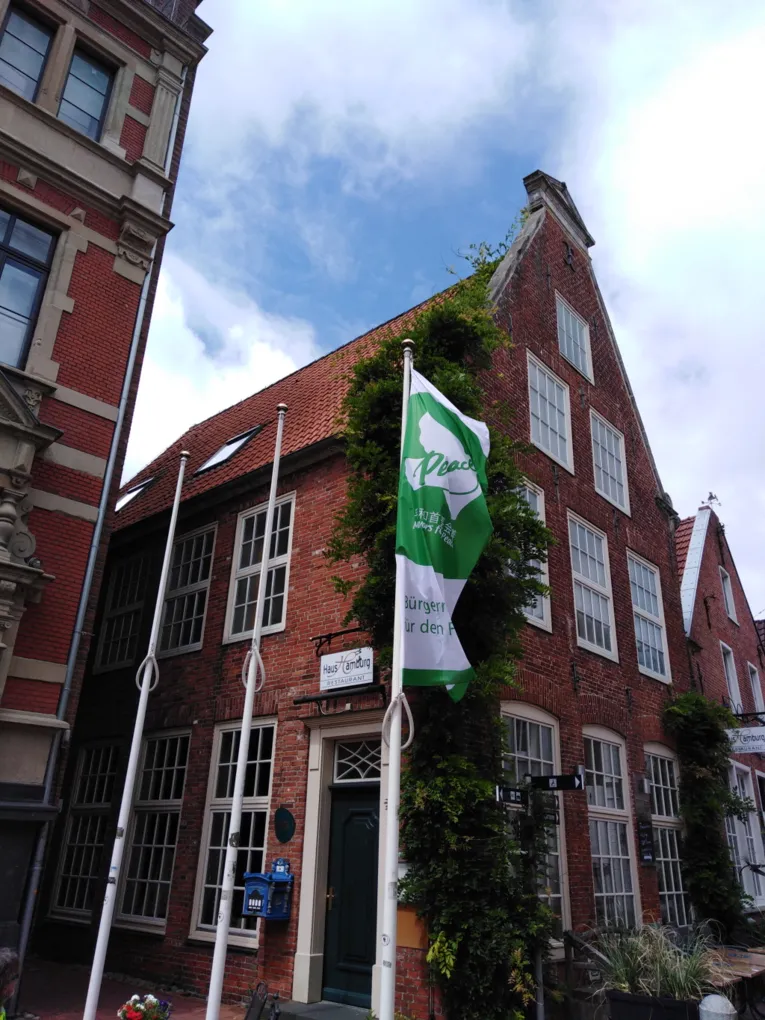 Die gr&uuml;n-wei&szlig;e Mayors-for-Peace-Flagge weht vor einem roten Backsteingeb&auml;ude in Leer (Ostfriesland) im Wind.